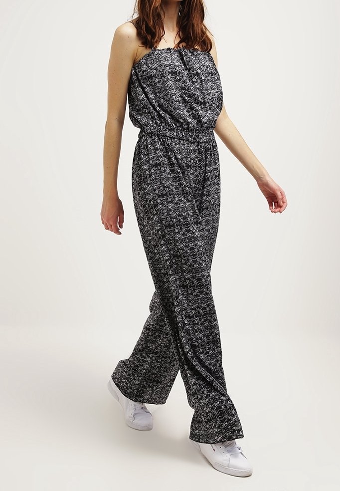 Combinaison à motifs noir et blanc avec un design sans bretelles, une taille élastique et une coupe large. Le mannequin porte des baskets blanches pour contraster.