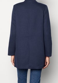 Chaqueta azul marino, de un solo pecho, manga larga, tela texturizada, dobladillo recto, diseño minimalista, sin cierres visibles ni patrones.