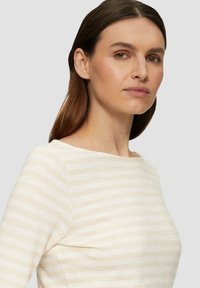 Top a maniche lunghe in tessuto leggero con un motivo a righe crema e beige chiaro. Collo rotondo e forma aderente.
