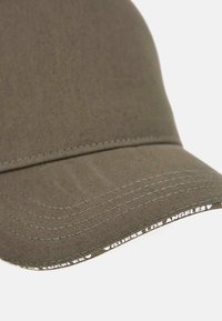 Cappellino da baseball verde oliva con visiera curvata, caratterizzato da cuciture tonali e un logo ricamato bianco lungo la parte inferiore della visiera.