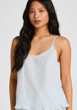 Jonge vrouw met lang zwart haar, gekleed in een lichtblauw gestreept mouwloos topje met ruchtrand en kanten afwerking bij de hals.