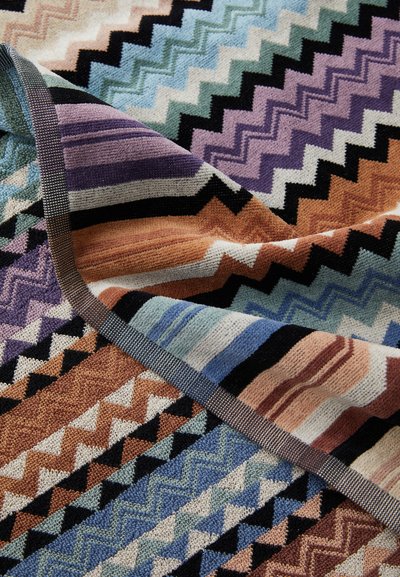 Coperta multicolore con un audace motivo a zigzag in tonalità di blu, viola, arancione e nero, con una superficie testurizzata e bordi solidi.