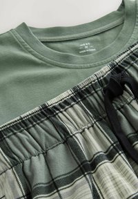 Grünes Baumwoll-T-Shirt mit einem karierten unteren Abschnitt in Schwarz- und Grautönen, mit einem gerafften Design und schwarzen Kordelzugdetails.