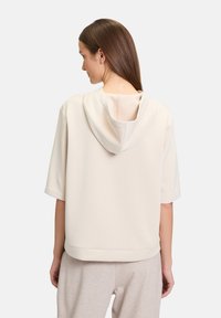 Jasno beżowy sweatshirt z kapturem i krótkimi rękawami, miękka tekstura oraz regulowany kaptur, zestawiony z jasno beżowymi spodniami.