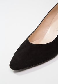 Escarpin noir en daim à bout pointu avec un intérieur beige lisse. Présente une silhouette élégante et une ouverture subtile sur le dessus.