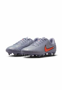 Crampons de football violets présentant un dessus texturé, un design nervuré et un swoosh Nike orange. Équipés de crampons moulés pour l'adhérence.