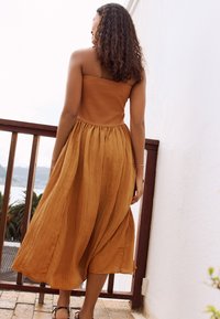 Pánt nélküli ruha égett narancssárga színben, szabott fazonú felsőrésszel és légies, bokáig érő szoknyával, texturált, könnyű anyagból.