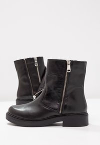 Czarne skórzane botki na kostkę z okrągłym noskiem, bocznymi zamkami i niskim, blokowym obcasem z widocznymi detalami szycia.