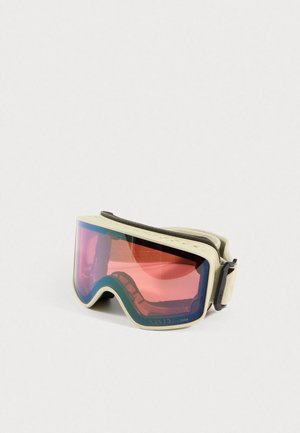 Lunettes de ski avec monture beige et lentille teintée en rouge, dotées d'une sangle crème ajustable, posées sur une surface blanche.
