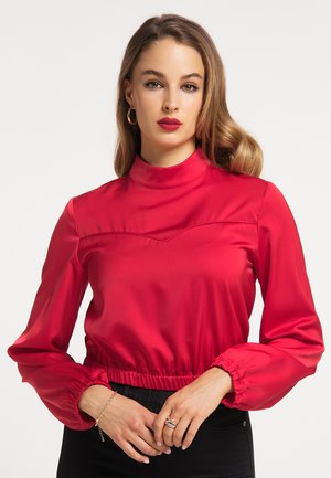 Bluză roșie din satin, cu guler înalt, mâneci bufante și talie elastică; are un design structurat și o textură netedă.
