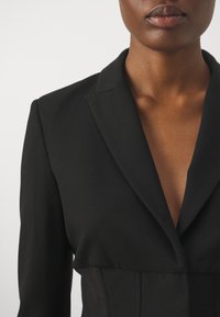 Black blazer with a tailored fit, sharp lapels, and plunging neckline. Smooth fabric texture with structured seams details.