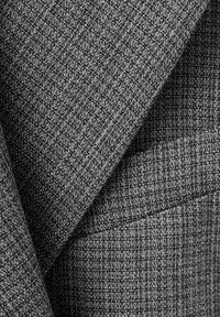 Gros plan d'un tissu gris texturé à tissage fin, montrant des couches pliées et des détails de couture.