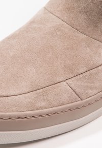 Gros plan sur l'avant d'une chaussure en daim beige avec des coutures visibles et un bord de semelle en caoutchouc.