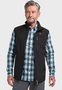 Schwarze Softshell-Weste über einem blauen und grünen karierter Hemd. Die Weste hat Reißverschlusstaschen und einen hohen Kragen. Button-down-Hemd mit langen Ärmeln.