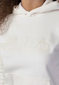 Felpa bianca con logo FILA testurizzato in un design tonale sobrio. Presenta un cappuccio con lacci e una tasca frontale.