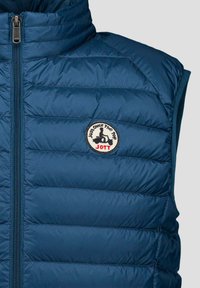 Chaleco acolchado azul marino con cuello alto, que presenta paneles acolchados horizontales, una cremallera frontal y un parche de logotipo redondo en el pecho.