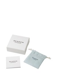 Scatola quadrata bianca con "SKAGEN DENMARK" stampato sopra, accompagnata da un sacchetto di tessuto blu chiaro e un piccolo opuscolo bianco.