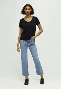 Μαύρη κοντομάνικη μπλούζα V-λαιμού συνδυασμένη με ανοιχτό μπλε ίσιες παντελόνες και μαύρα παπούτσια. Το μοντέλο στέκεται με τα χέρια στις τσέπες.