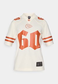 Kermavärviga NFL jersy, millel on punased triibud varrukatel ja ees suur "60" punase värviga, koos meeskonna logoga ja siltidega hems.