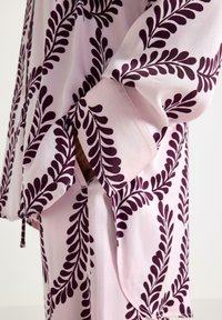 Lys pink pyjamasæt med et dybt lilla bladmønster. Glat stof med en afslappet pasform og brede ærmer. Markant kontrast i farverne.