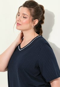 Námořnické modré tričko s krátkým rukávem s bílými puntíky a dekorativním bílým výstřihem. Hladká tkanina a volný střih.