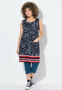 Kelloton kudonnut sininen mekko abstraktilla valkoisella ja harmaalla kuviolla, jossa on kiinteä punamustaraidallinen helma. Yhdistetty teal-värisiin capri-housuihin ja mustiin lenkkareihin.