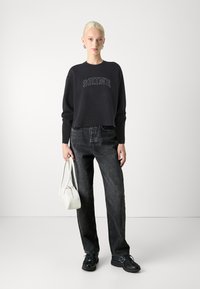 Svart cropped sweatshirt med "SHINE" trykt i hvitt, kombinert med mørkegrå jeans, en hvit håndveske og svarte joggesko.