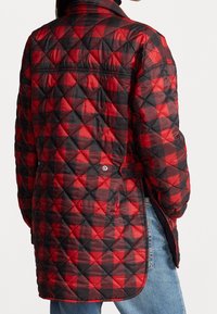 Giacca trapuntata in un motivo a scacchi rosso e nero, con colletto alto, tasche laterali e chiusure a scatto. Materiale resistente con una finitura texturizzata.
