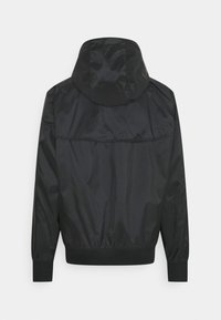Černá kapuce jacket vyrobená z lesklého nylonu. Má elastické manžety a lem, s viditelným švem přes záda. Texturovaný povrch.
