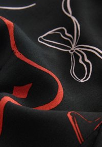 Materialul negru cu o textură netedă prezintă modele abstracte albe și roșii, inclusiv un fluture și linii ondulate, creând un design îndrăzneț.