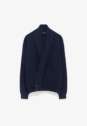 Cardigan en maille bleu marine avec un col châle, un design oversize et trois boutons sur le devant. Motif texturé sur l'ensemble.