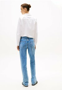 Chemise blanche à manches longues avec un col, assortie à un jean évasé bleu clair. Tissu lisse avec des détails légèrement usés sur le jean.