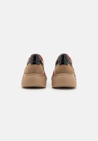 Brown and black sneakers with a textured surface, featuring red accents and a padded heel. Rubber sole with a patterned outsole.