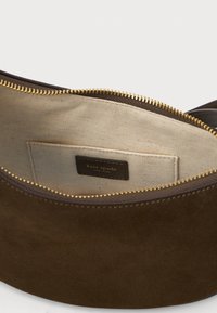 Bolsa de camurça castanha com fecho dourado parcialmente aberta, mostrando um bolso interior em tecido bege com o rótulo "kate spade new york".