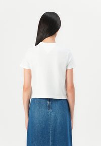 T-shirt blanc court à manches courtes, avec un col rond et une texture lisse. Porté avec une jupe en denim bleue.