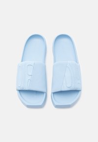 Ανοιχτό μπλε σλάιντ σανδάλια με ανάγλυφη επάνω ζώνη σε σχήμα σταυρού και επίπεδο σόλα. Το υλικό φαίνεται λείο, με ανάγλυφο σχέδιο στη ζώνη.