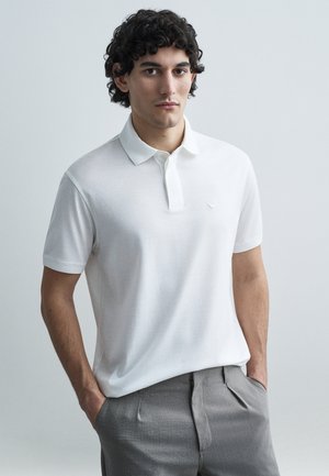 Λευκό πόλο μπλουζάκι με υφασμάτινο γιακά και μικρό κεντημένο λογότυπο· σετ με γκρι, ραμμένο παντελόνι. Λείο φινίρισμα υφάσματος.