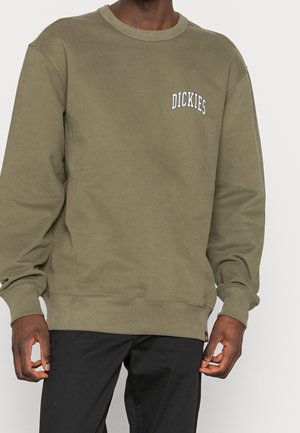Sweatshirt vert olive avec des poignets et un ourlet côtelés, arborant un logo brodé blanc sur la poitrine. Fabriqué en coton doux.