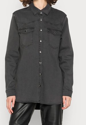 Black denim shirt with a collar, long sleeves, snap button closure, and two chest pockets. Subtle faded texture. Worn over black leather pants.