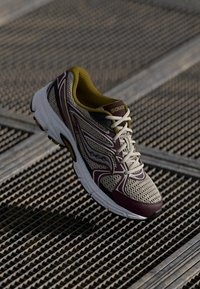 Chaussure de course avec une tige en maille beige, accents bordeaux et intérieur jaune. Équipée de lacets blancs et d'une semelle rembourrée.