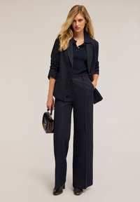 Blazer marin și pantaloni largi, țesătură texturată, cu un top ribbed în nuanță marin. Accesoriu: geantă mică neagră. Pantofii cu toc înalt completează ținuta.