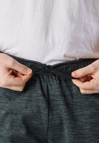 Gray athletic shorts with a textured fabric, featuring a black drawstring at the waist. A person is tying the drawstring.