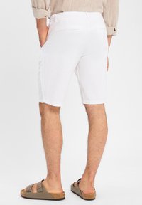 Shorts bianchi in lino con vita elastica, tasche laterali e orli arrotolati, abbinati a sandali marroni con due cinturini.