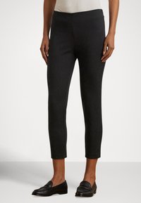Melnas, potītes garuma bikses ar gludu tekstūru un piegulošu dizainu. Kombinētas ar melniem loaferu apaviem, attēlotas uz neitrālas krāsas fona.