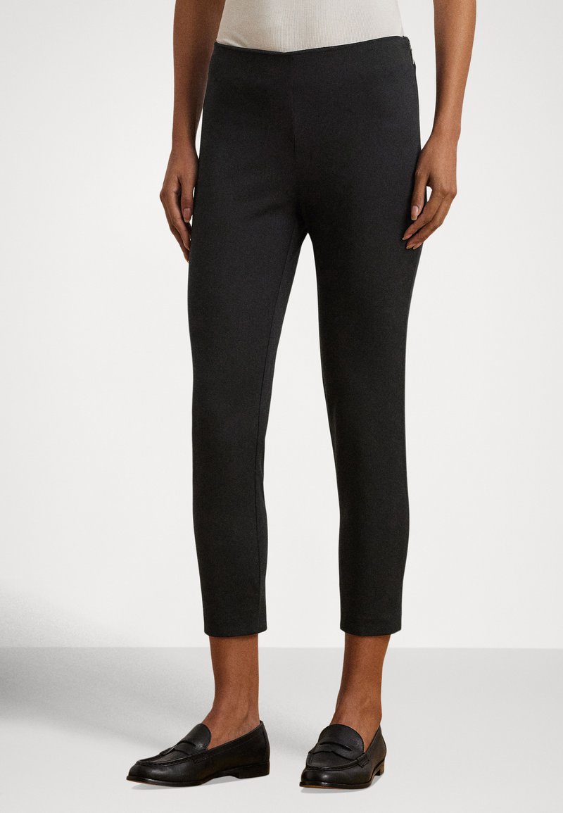 Melnas, potītes garuma bikses ar gludu tekstūru un piegulošu dizainu. Kombinētas ar melniem loaferu apaviem, attēlotas uz neitrālas krāsas fona.