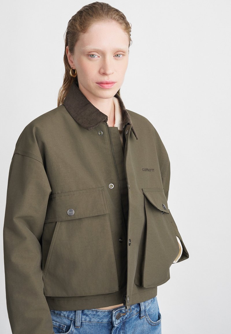 Olivengroen cropped jack met een ribbelkraag, drukknopen aan de voorkant en twee grote zakken. Gemaakt van duurzaam katoen.