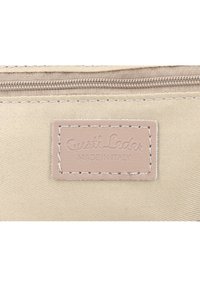 Beige tygpåsar med en slät läderetikett. Etiketten har texten "Gusti Leder MADE IN ITALY" och är accentuerad med ljusa sömmar. Dragkedja synlig.