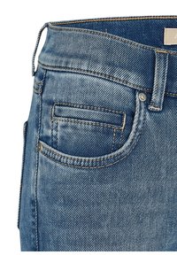 Jeans in denim blu con un design aderente, lavaggio chiaro, cuciture in rame e una piccola tasca frontale con dettagli in rivetto metallico.