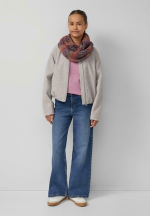 Young person standing, wearing gray zip-up jacket, purple knit scarf, pink shirt, wide-leg blue jeans, and white sneakers against gray wall.