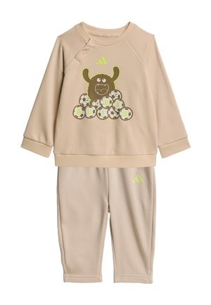 Survêtement beige pour tout-petit avec un haut à manches longues présentant un monstre de dessin animé, des ballons de football formant le mot "ADIDAS" et un pantalon assorti avec logo.